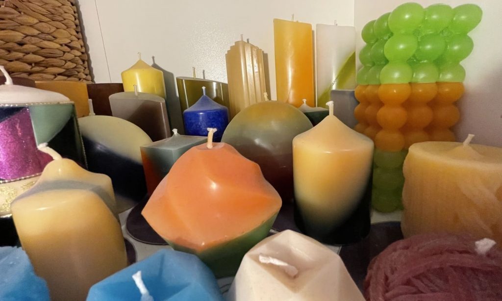 viele verschiedenen selbstgegossene Kerzen dicht zusammen im Schrankfach